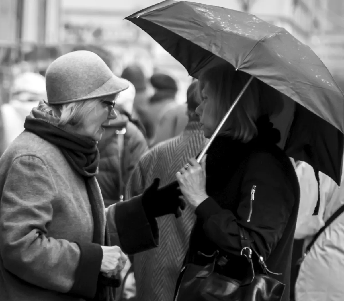 Two older women talking beneath umbrellas in black and white